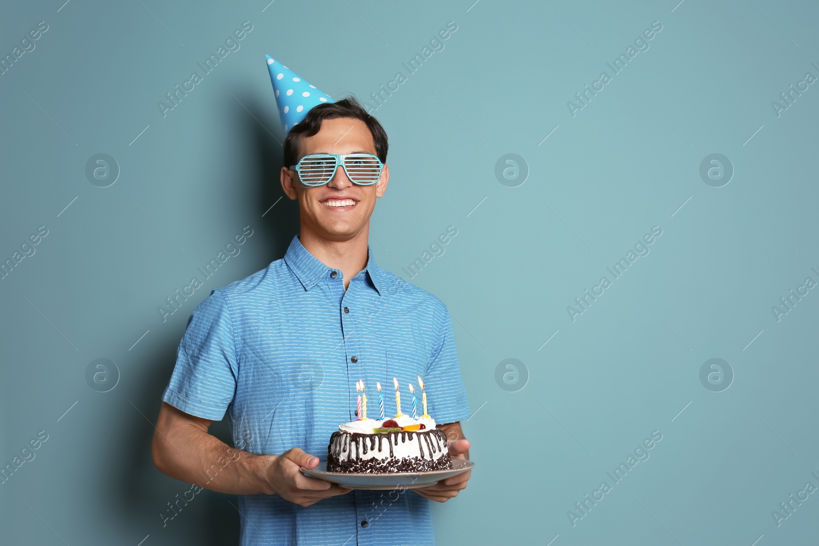 Photo of Young man with birthday cake on color background