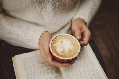 Woman with cup of coffee reading book at home, closeup