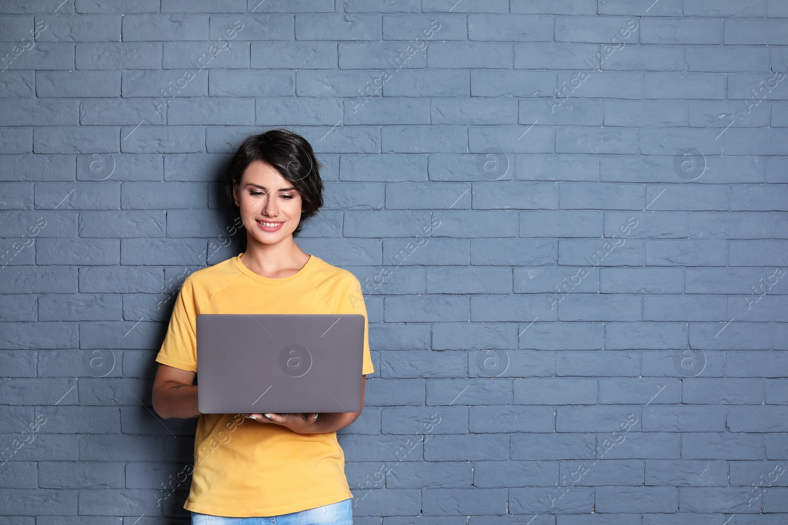 Photo of Young woman with modern laptop on brick wall background