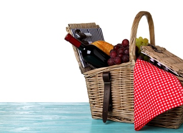 Wicker picnic basket with wine and different products on wooden table against white background, space for text