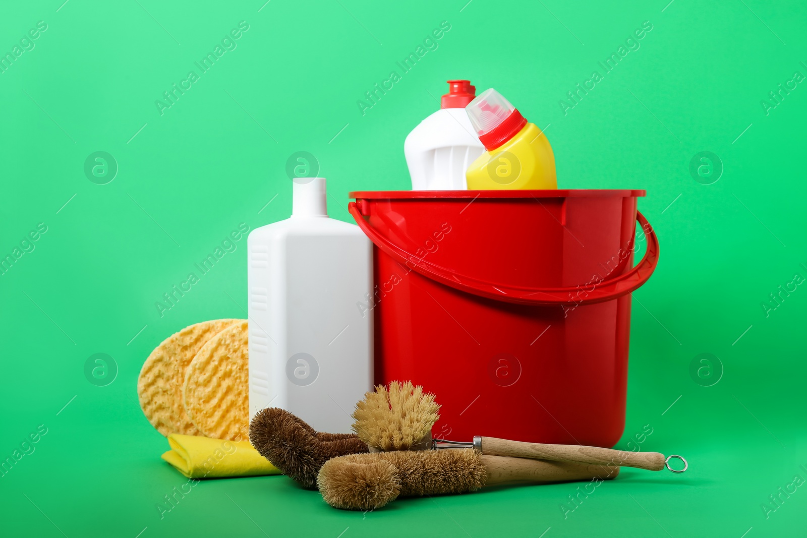 Photo of Red bucket, cleaning supplies and tools on green background