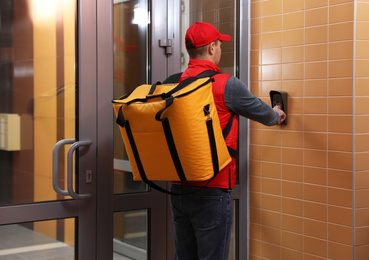 Photo of Male courier with thermo bag pushing intercom button. Food delivery service