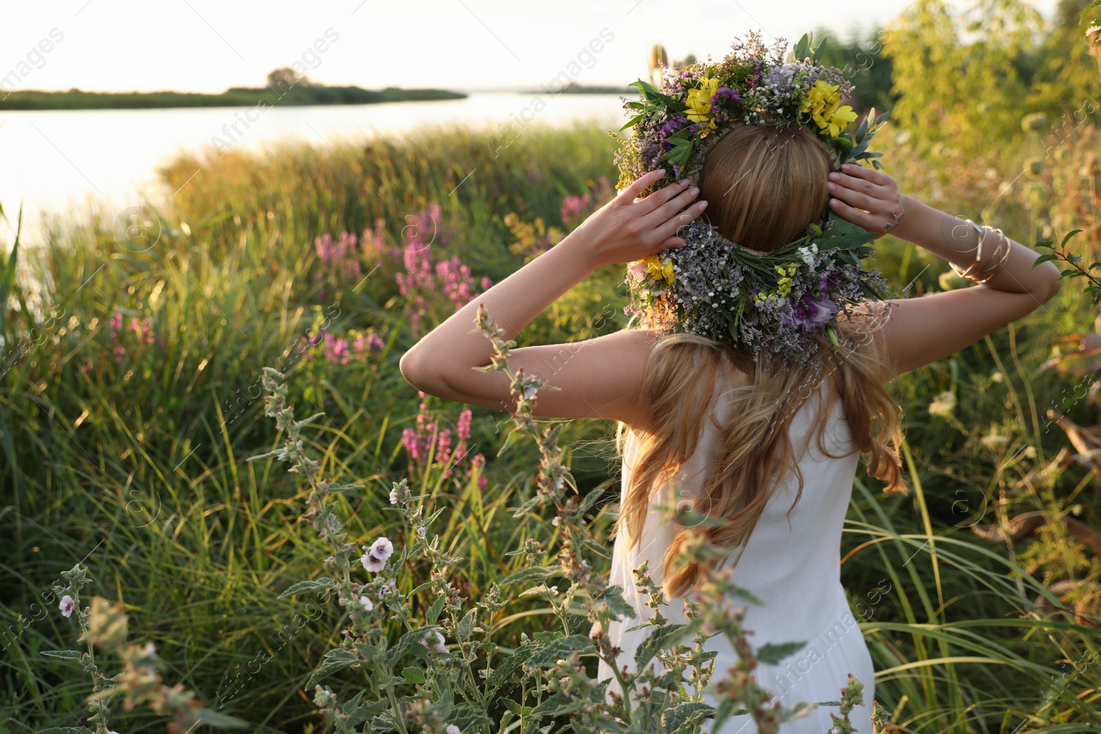 Photo of Young woman wearing wreath made of beautiful flowers outdoors on sunny day