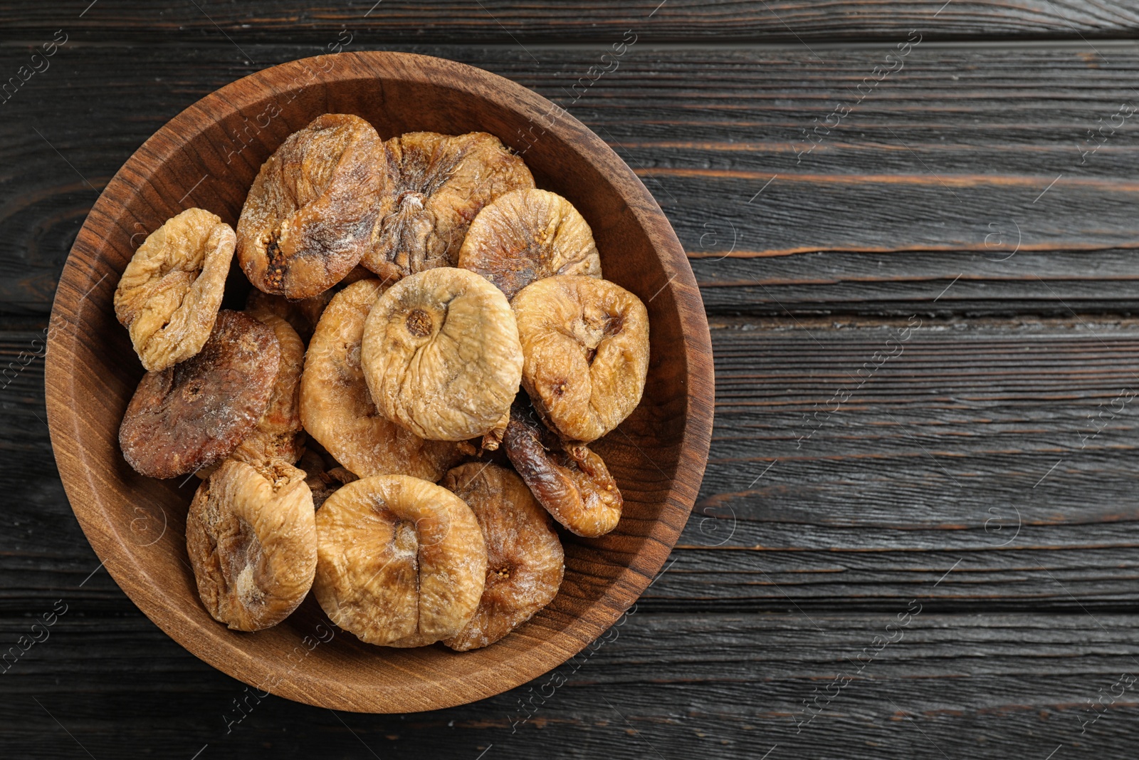 Photo of Wooden bowl of tasty dried figs on black table, top view. Space for text