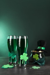 Photo of St. Patrick's day celebration. Green beer, leprechaun hat, pot of gold and decorative clover leaves on grey table. Space for text