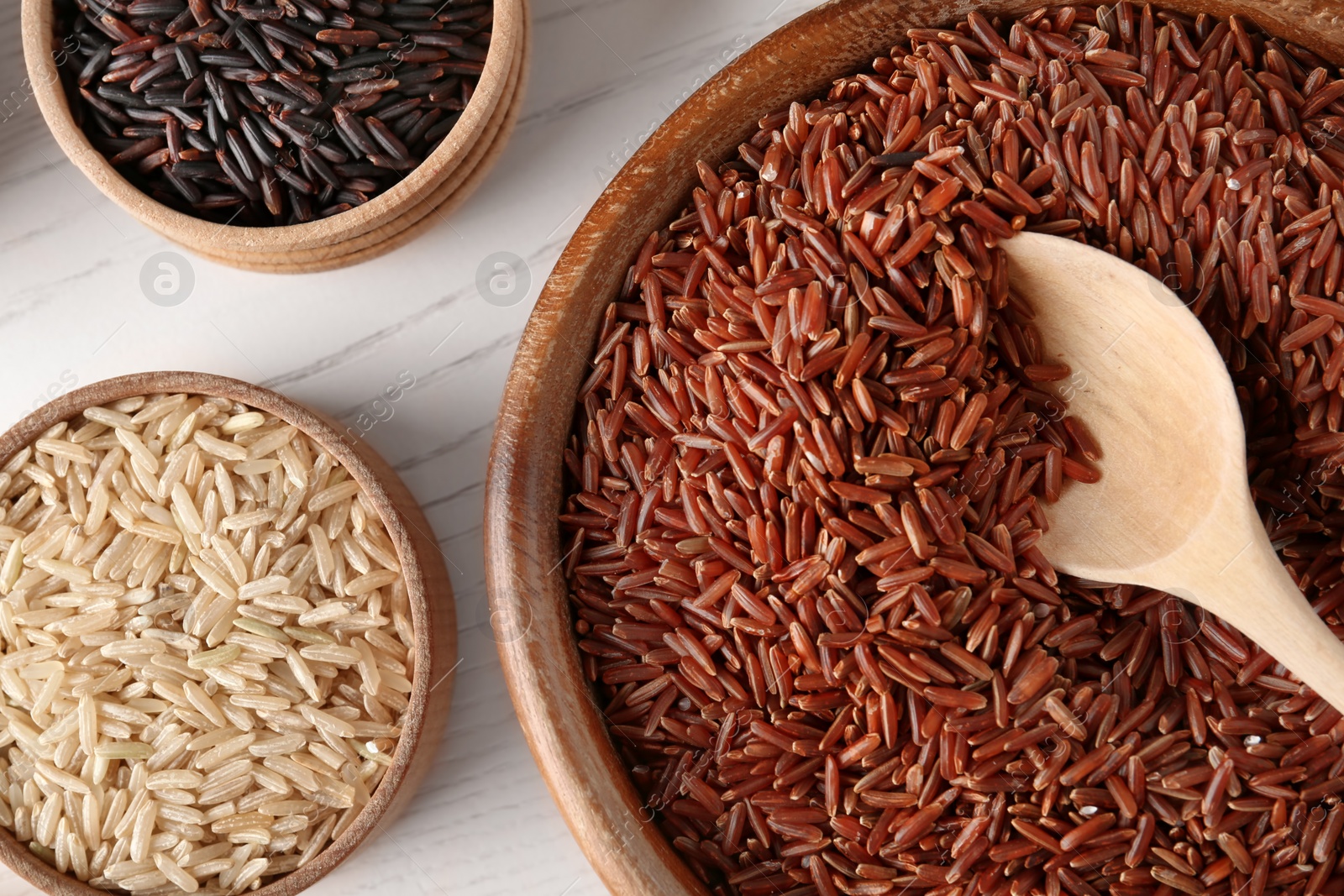 Photo of Flat lay composition with brown and other types of rice in bowls on white wooden background