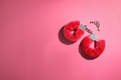 Photo of Red furry handcuffs and keys on pink background, flat lay with space for text. Sex toy