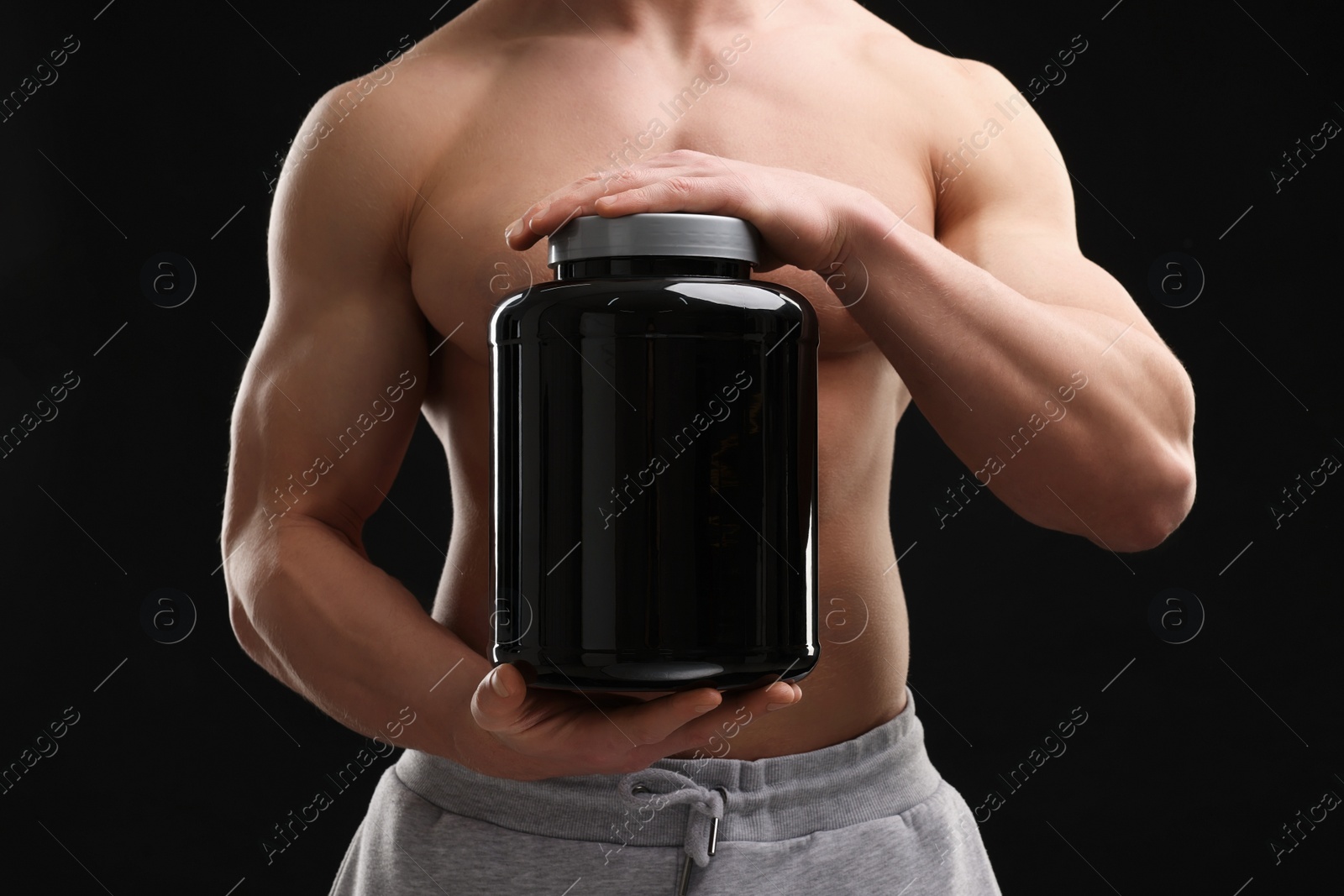 Photo of Young man with muscular body holding jar of protein powder on black background, closeup