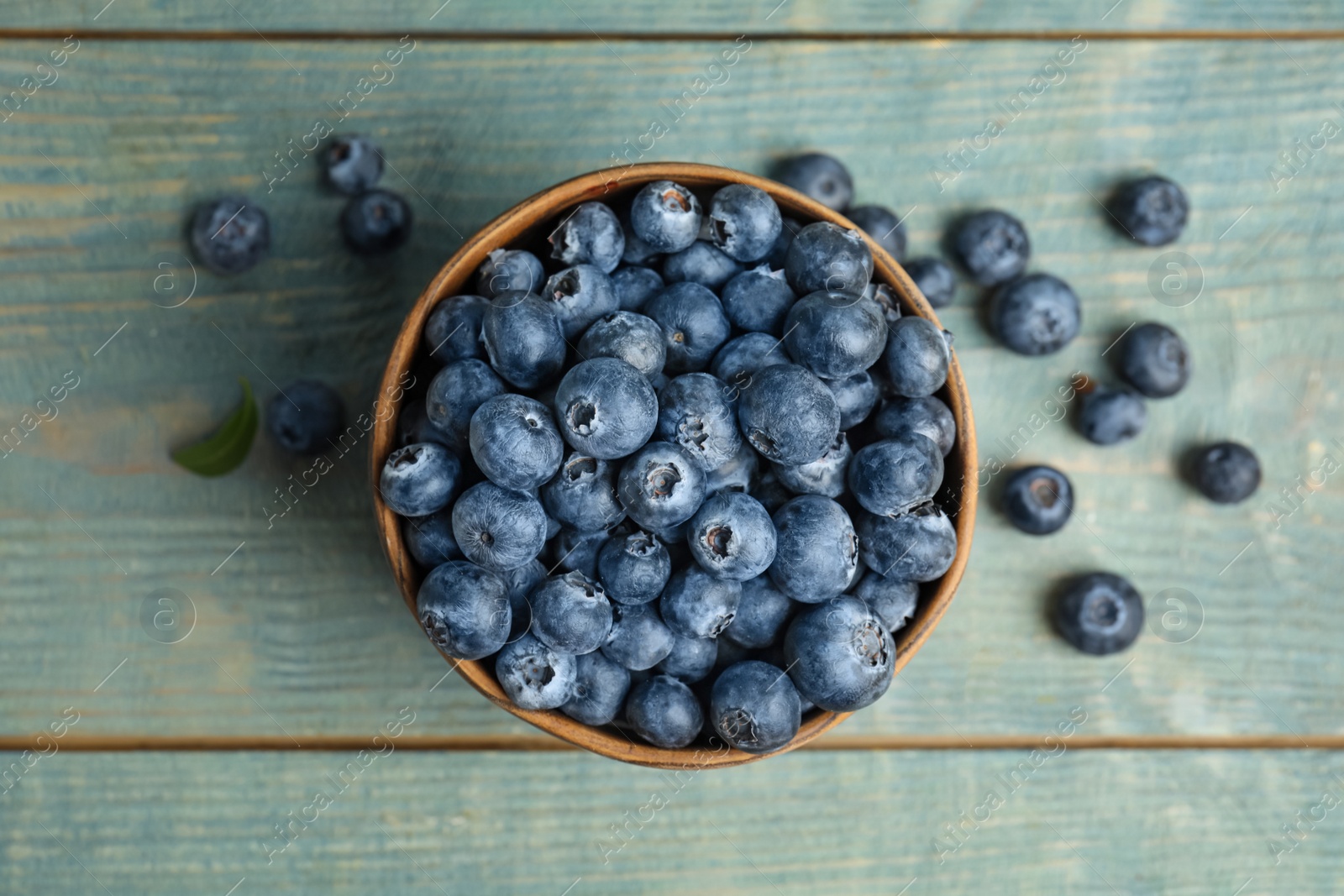 Photo of Fresh ripe blueberries in bowl on wooden table, flat lay