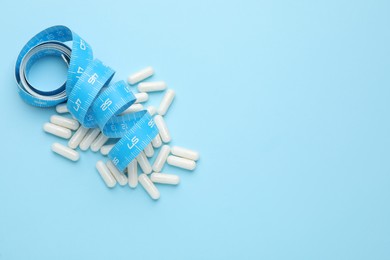 Photo of Weight loss pills and measuring tape on light blue background, flat lay. Space for text