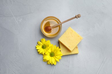 Photo of Natural beeswax, honey and flowers on light grey stone table, flat lay