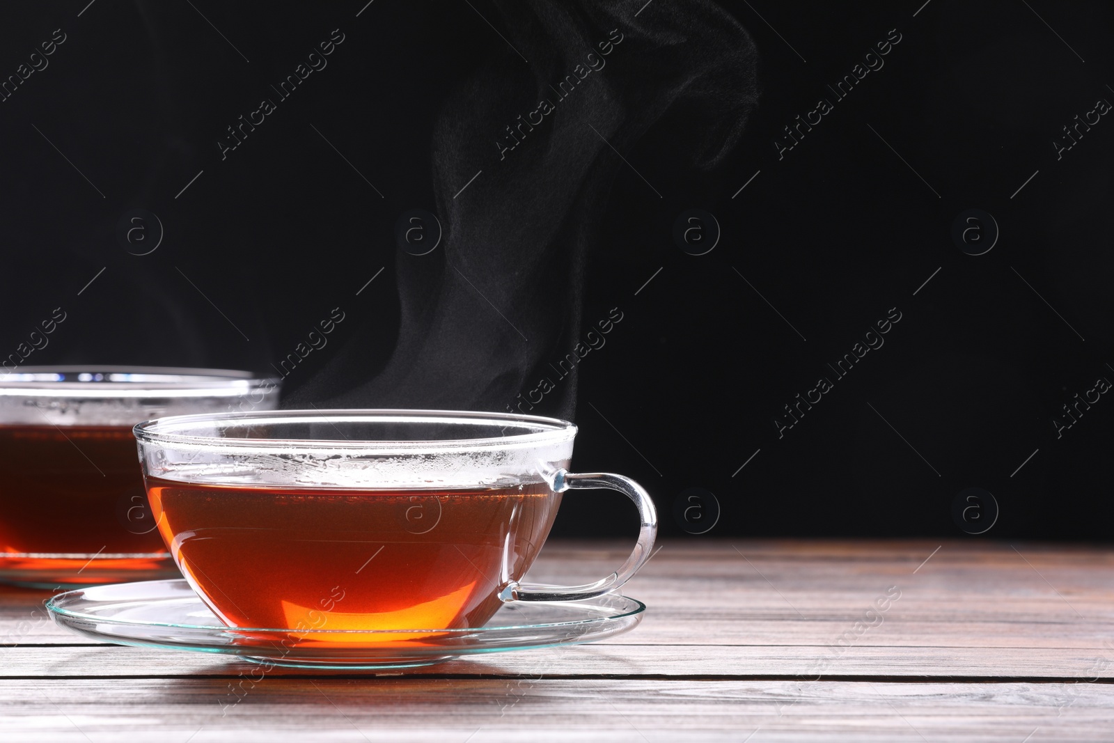 Photo of Glass cups with tea on wooden table against black background, space for text