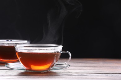 Photo of Glass cups with tea on wooden table against black background, space for text