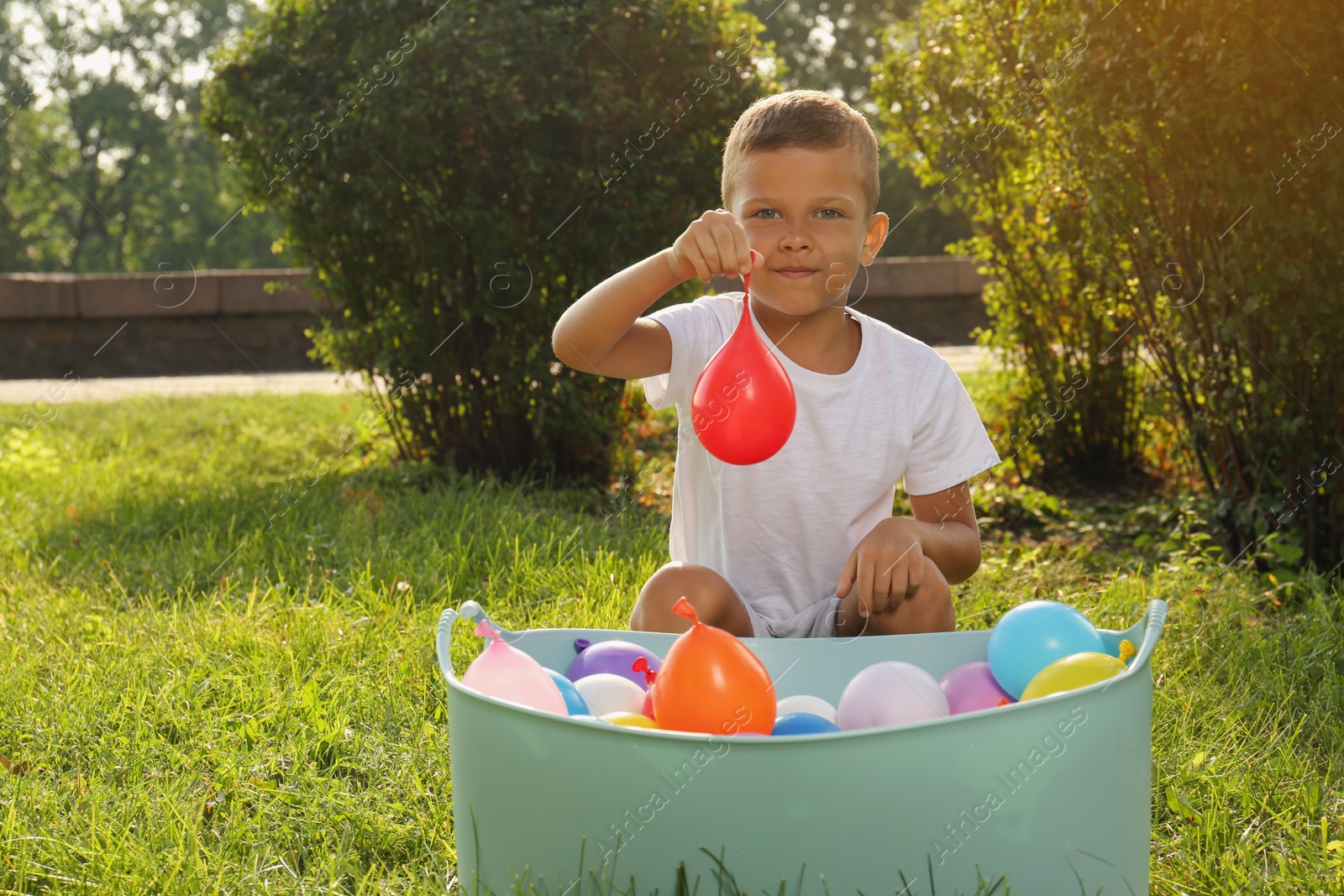 Photo of Little boy with basin of water bombs in park