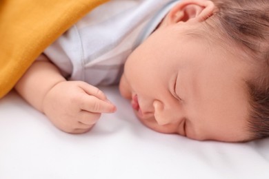 Cute newborn baby sleeping under orange blanket on bed, closeup
