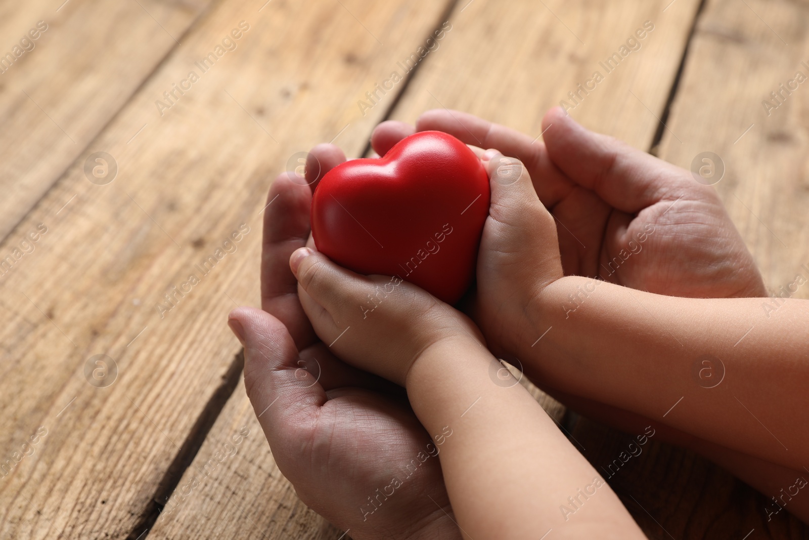 Photo of Father and his child holding red decorative heart at wooden table, closeup