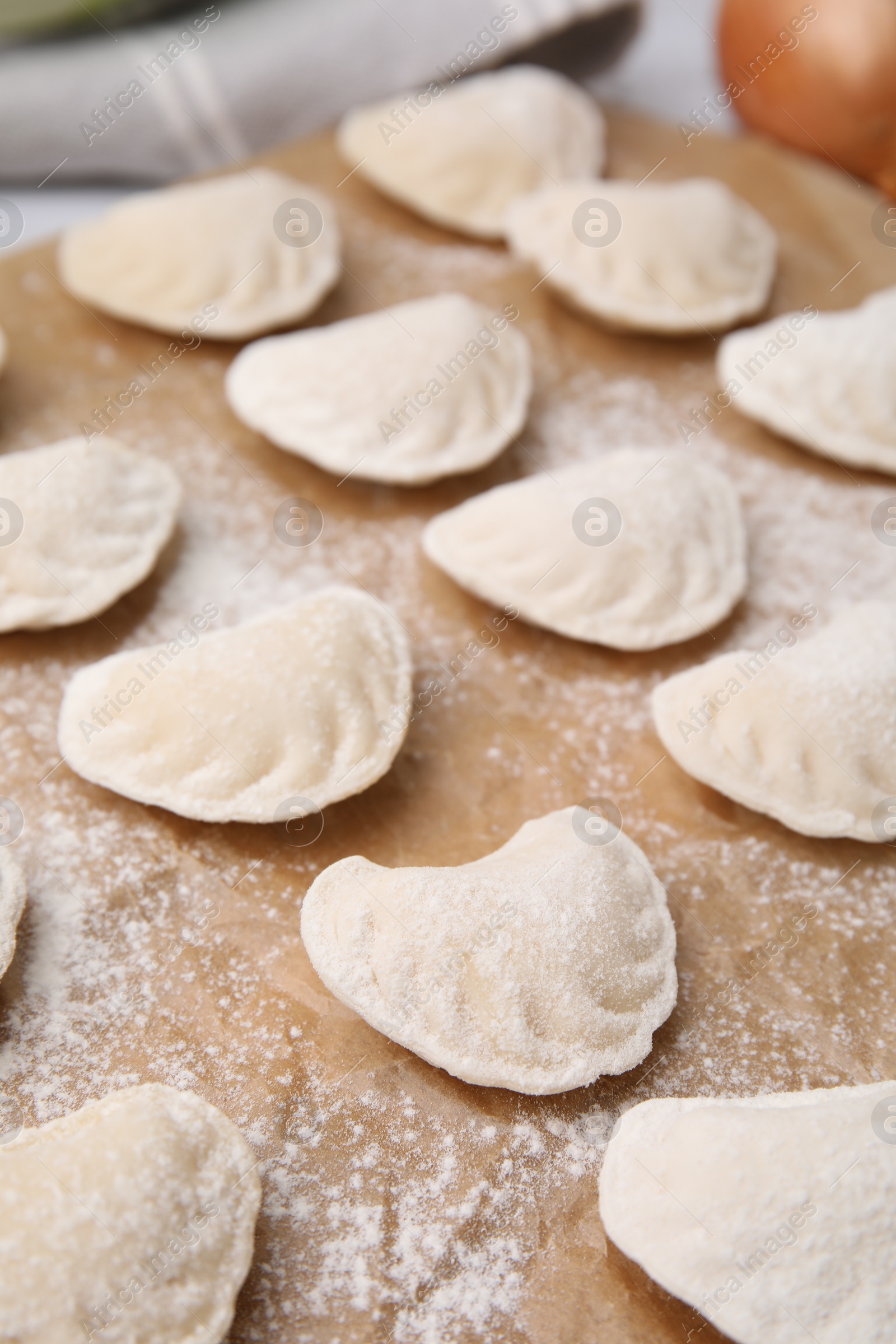 Photo of Raw dumplings (varenyky) with tasty filling and flour on parchment paper, closeup view
