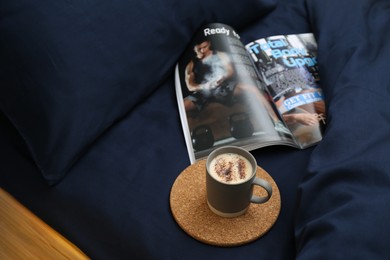 Photo of Open magazine and cup of coffee on bed with stylish silky linens, above view
