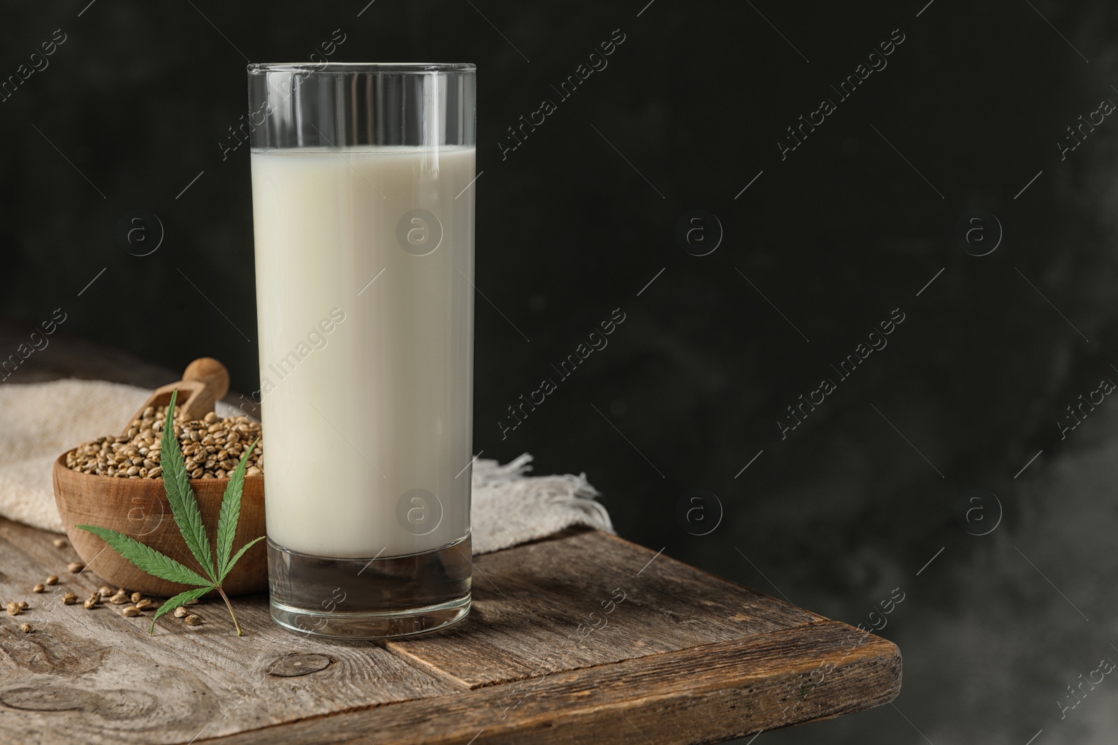 Photo of Composition with glass of hemp milk on wooden table against dark background. Space for text