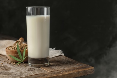 Photo of Composition with glass of hemp milk on wooden table against dark background. Space for text