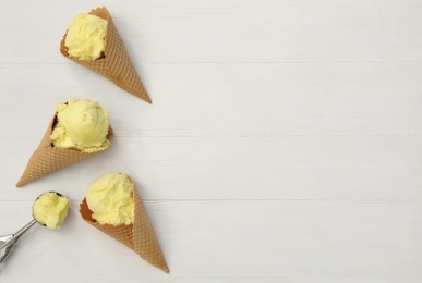 Photo of Yellow ice cream in wafer cones and scoop on white wooden table, flat lay. Space for text