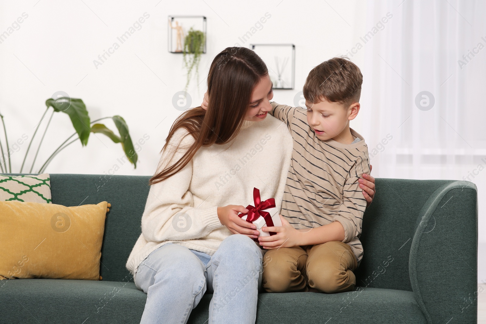 Photo of Little boy presenting his mother with gift on sofa at home