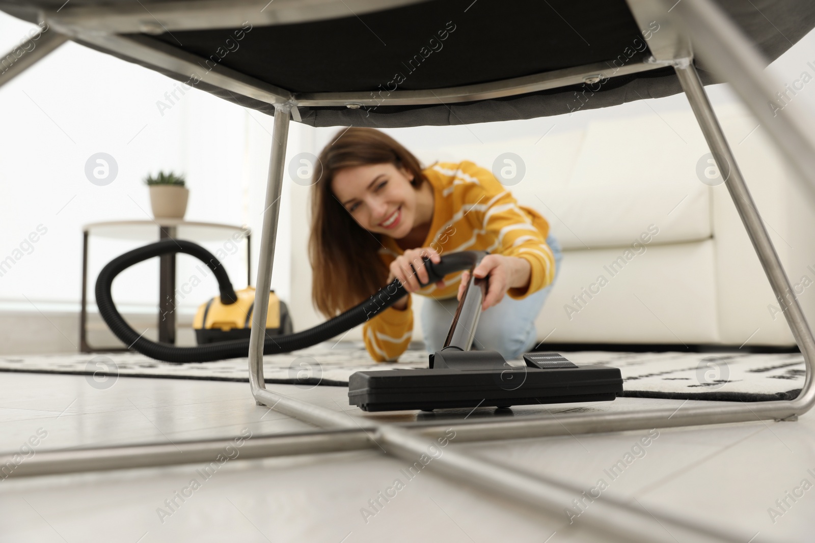 Photo of Young woman using vacuum cleaner at home