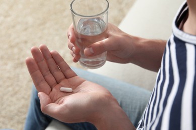 Man with glass of water and pill on blurred background, closeup