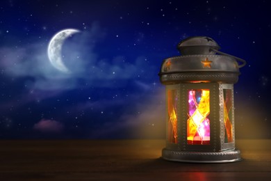 Image of Beautiful decorative Arabic lantern on wooden table at night, space for text. Fanous as Ramadan symbol