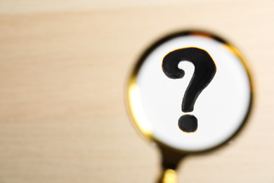 Photo of Question mark on beige background, view through magnifier glass. Space for text