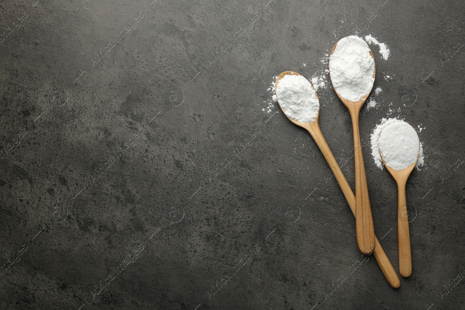 Photo of Baking powder in spoons on grey textured table, flat lay. Space for text