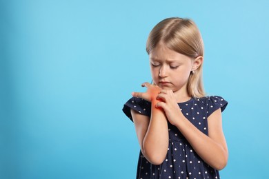 Photo of Suffering from allergy. Little girl scratching her hand on light blue background, space for text