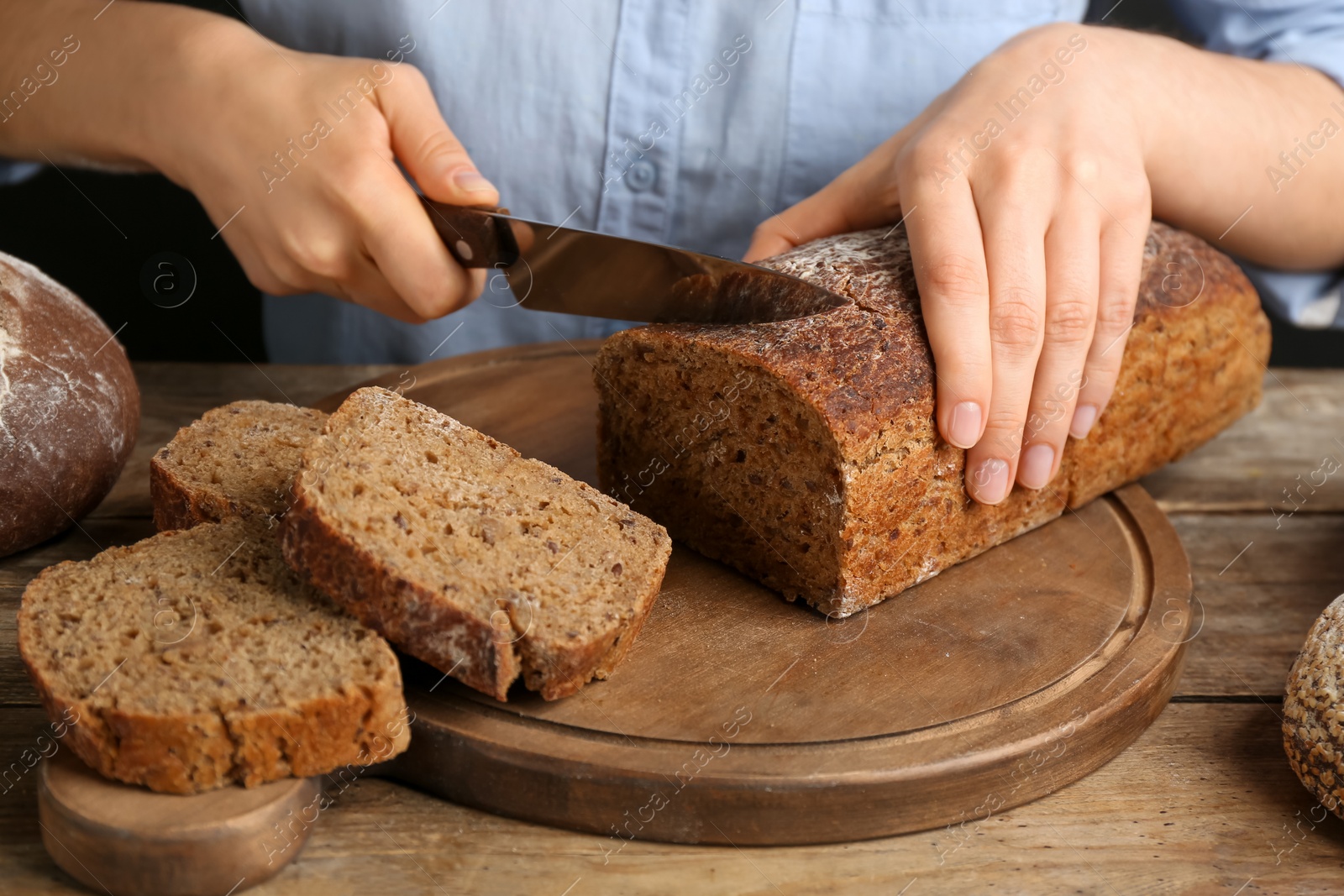 Photo of Woman cutting freshly baked bread at wooden table, closeup