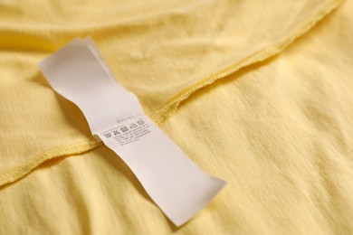 Photo of Clothing label on beautiful yellow garment, closeup. Space for text