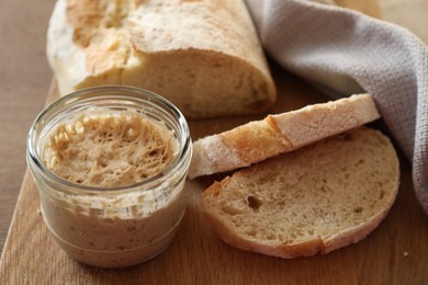 Photo of Sourdough starter in glass jar and bread on table, closeup