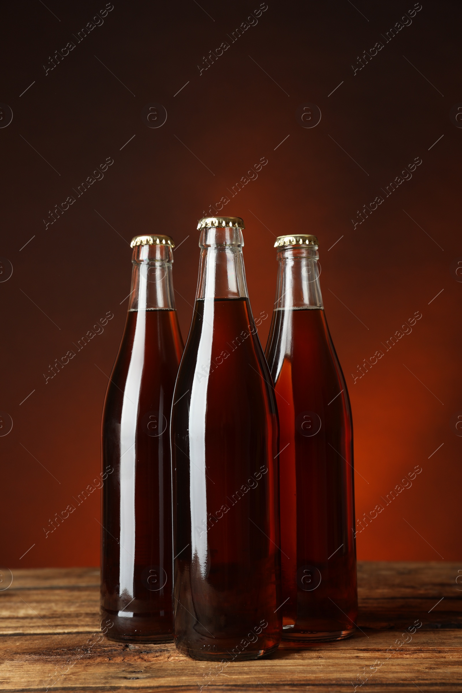 Photo of Bottles of delicious kvass on wooden table against brown background