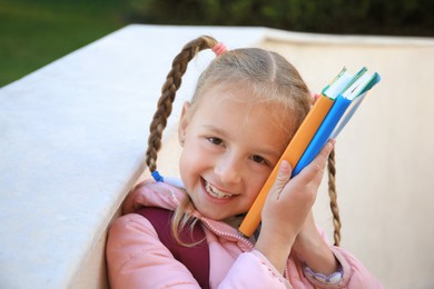 Photo of Cute little girl with backpack and textbooks outdoors