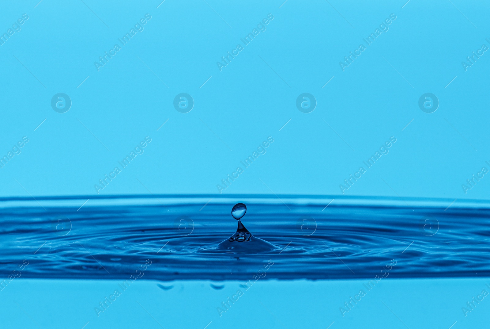 Photo of Splash of clear water with drop on blue background, closeup