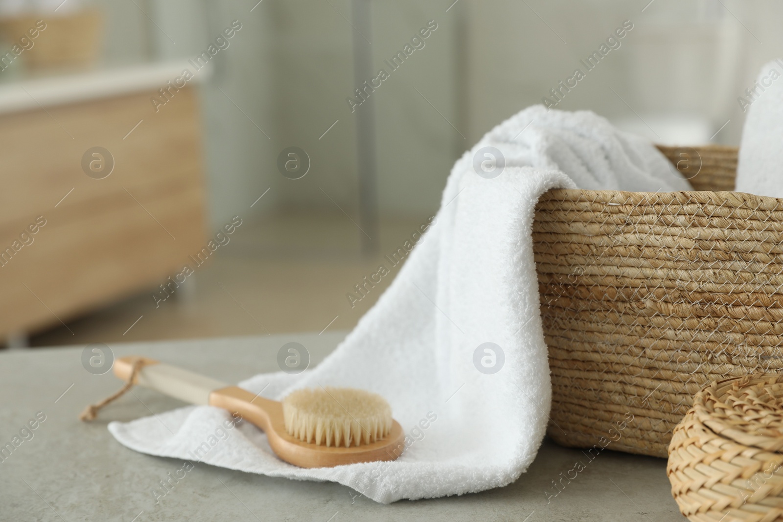 Photo of Wicker basket with clean towel and massage brush on table in bathroom