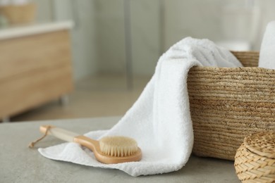 Wicker basket with clean towel and massage brush on table in bathroom