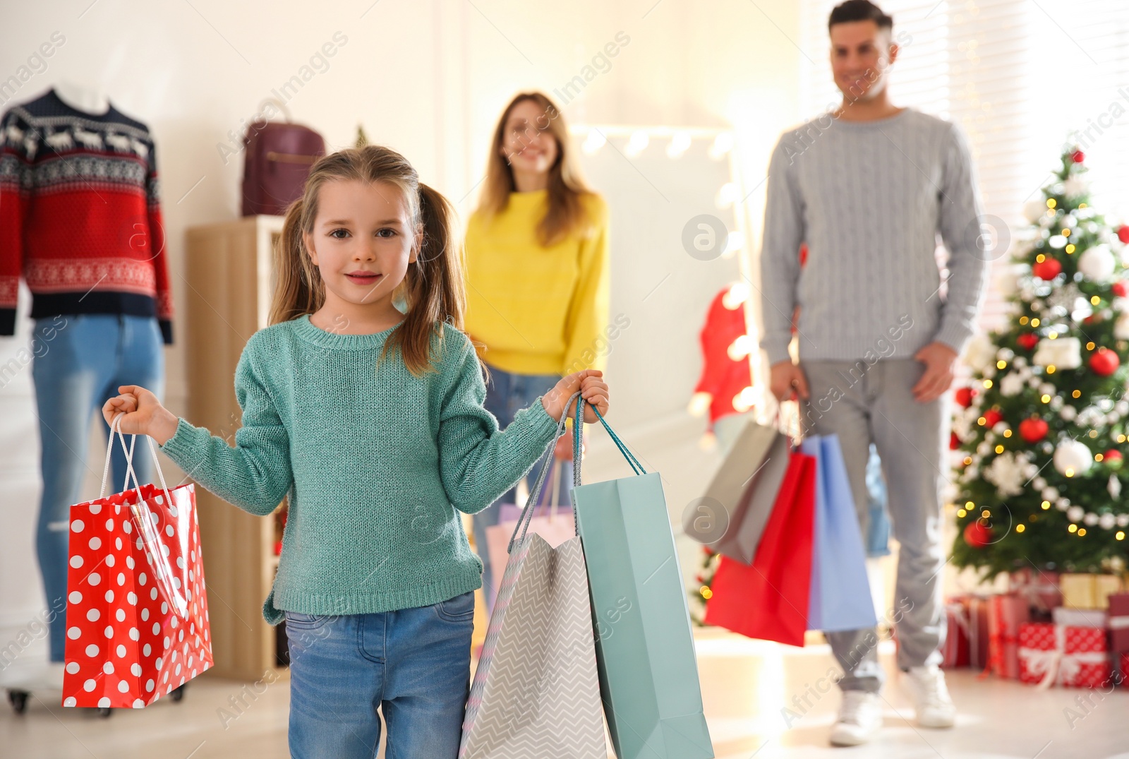 Photo of Little girl with bags near her parents in store. Family Christmas shopping