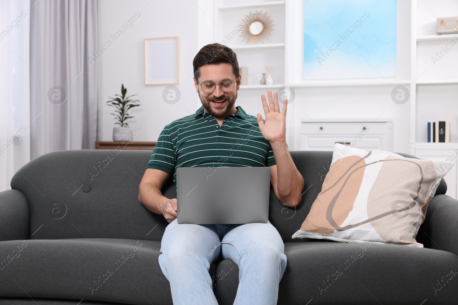 Photo of Happy man greeting someone during video chat via laptop at home