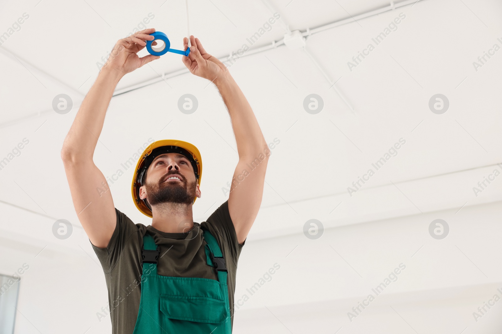 Photo of Electrician fixing wires with insulating tape indoors