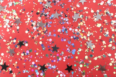 Photo of Shiny glitter on red background, flat lay