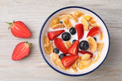 Photo of Bowl of tasty crispy corn flakes with milk and berries on wooden table, flat lay
