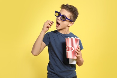 Boy with 3D glasses and popcorn during cinema show on color background