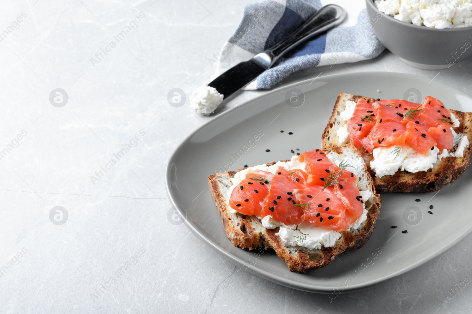 Photo of Delicious sandwiches with cream cheese, salmon and black sesame seeds on light grey table. Space for text