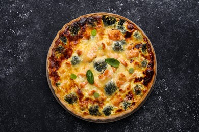Photo of Delicious homemade quiche with salmon and broccoli on black table, top view