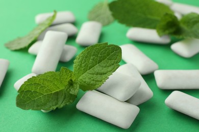 Tasty white chewing gums and mint leaves on green background, closeup