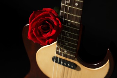 Photo of Beautiful rose near electric guitar on black background, closeup